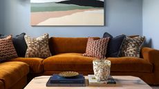 living room with blue walls, artwork, orange l-shaped sofa with lots of cushions and coffee table styled with books and vase