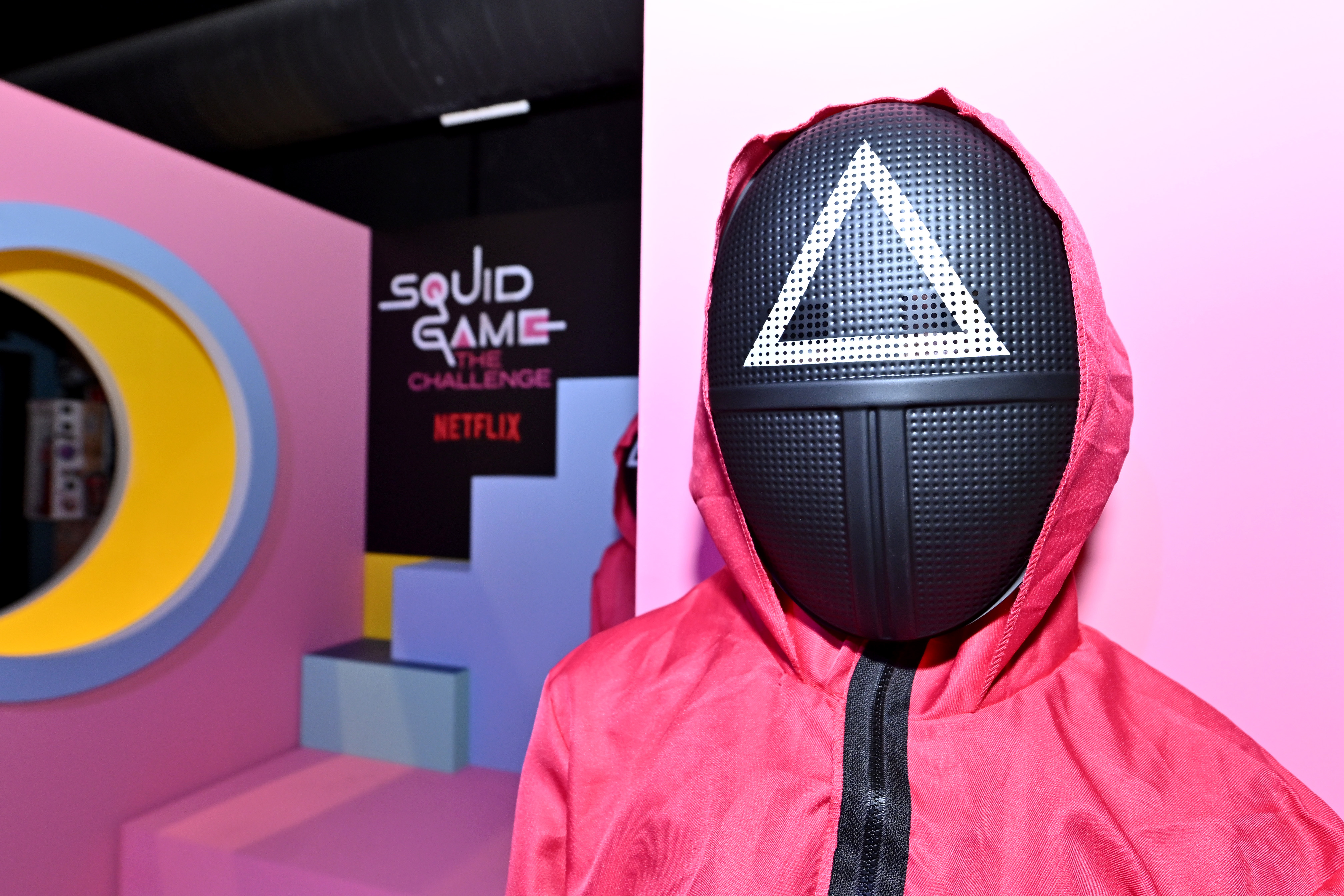 a person in a mask and suit from squid game standing by a course in the tv show Squid Game: The Challenge
