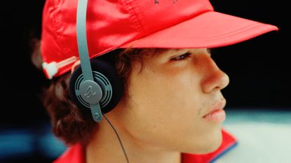 A young male-presenting person in a red cap with a pair of Gadhouse Wesley headphones over the top of it.