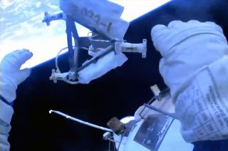 cosmonaut Sergey Prokopyev discards an old science experiment during a spacewalk, with the curve of earth visible in the background