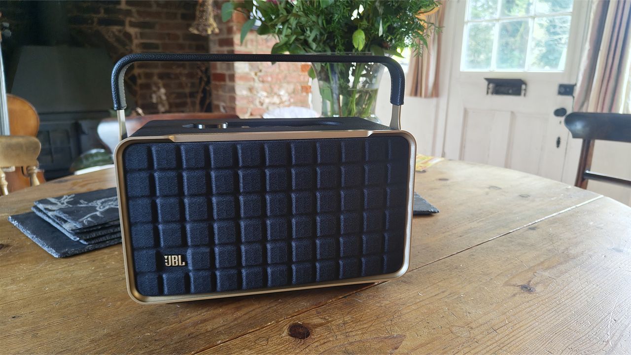 A black JBL Authentics 300 wireless speaker on a wooden table. The handle is extended upwards and there is a plant visible in the background.