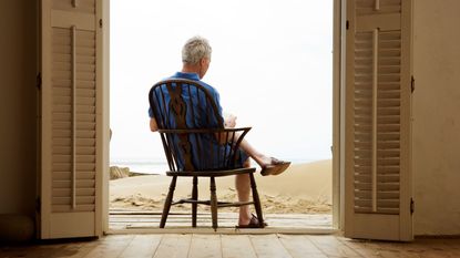 A man sits on a chair in a house on the beach. 