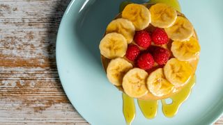 Pancake stack with banana and raspberries covered with maple syrup