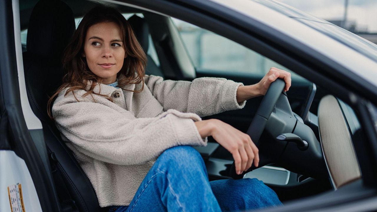 a woman in a car with one hand on the steering wheel