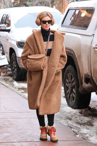 Nicky Hilton wears fur earmuffs, a brown and tan striped sweater, a teddy coat, a fur bag, black leggings, and combat ankle boots.