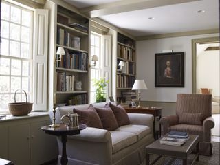 A library with custom built bookshelves and shutters and neutral walls and upholstery