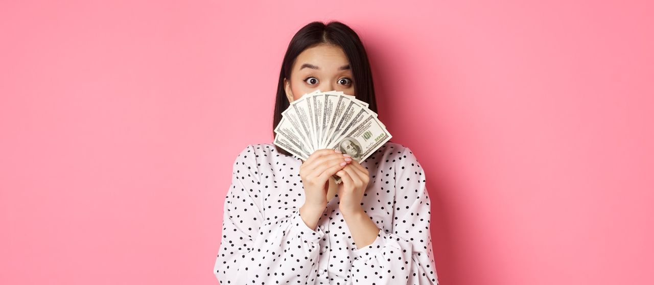 money saving apps - portrait of woman holding paper currency against pink background