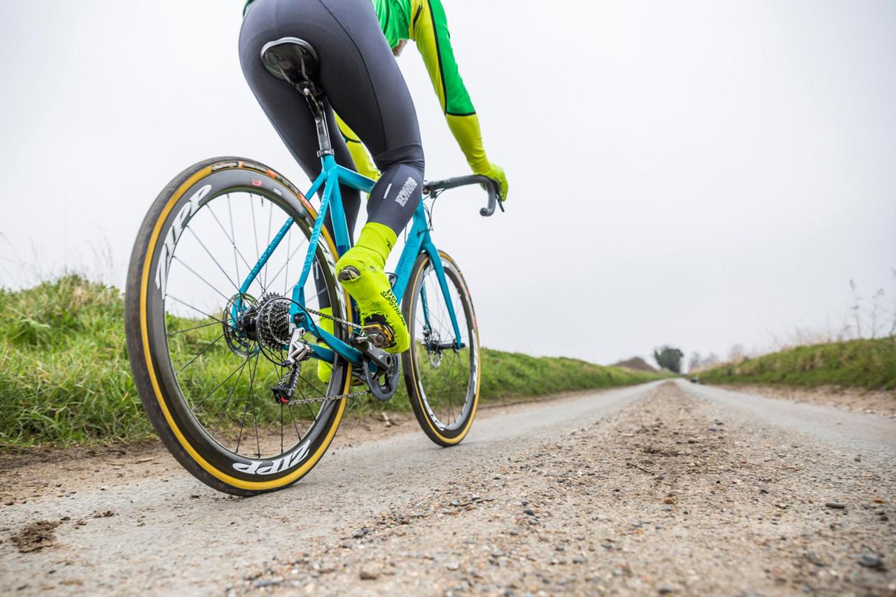 Cyclist riding a British B-road in the winter with dirt up the middle, with a bright jersey and fluorescent overshoes on. 