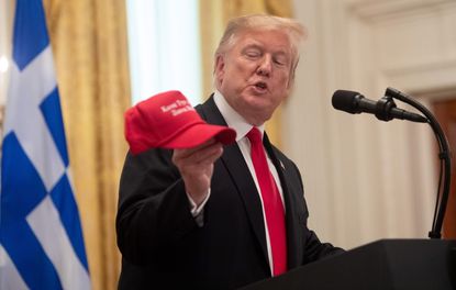 Trump holds up a Greek-language MAGA hat