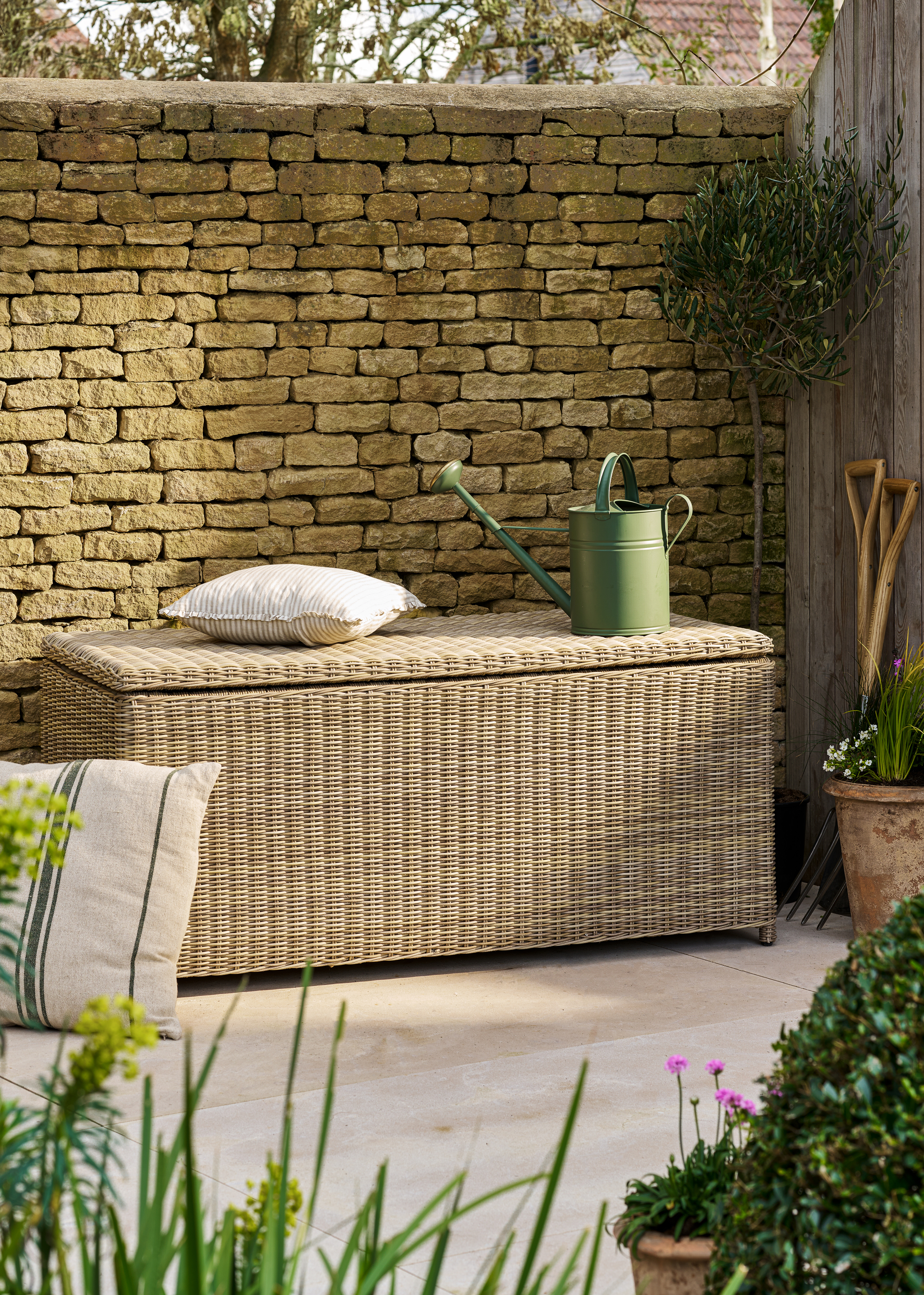 A garden patio with a wicker storage bench against a brick wall