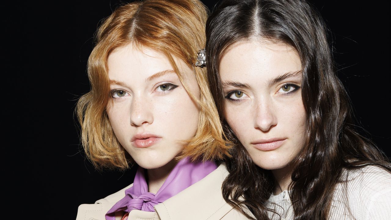 two models with blurred skin and wavy hair backstage at fashion week