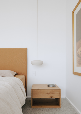 A minimalist bedroom with a silver tray on a nightstand, above the nightstand is a hanging pendant light.