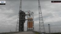 an orange and white rocket stands on the launch pad under cloudy gray skies