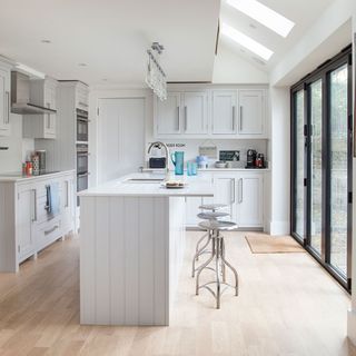 A white kitchen with a small island and metal bar stools
