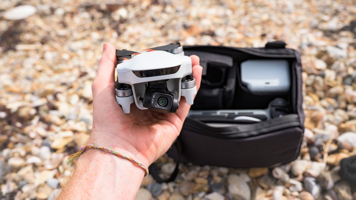 Potensic Atom 3 beginner drone in user's hands with its propellors folded away and the Fly More Combo bag and its content behind it, on a pebble beach