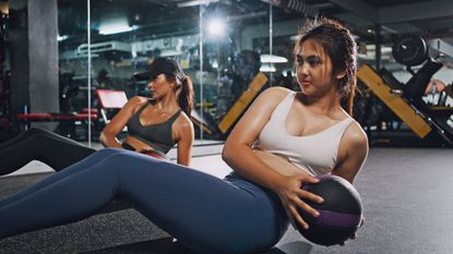 Group of women doing weighted Russian twists in a gym