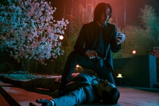 Keanu Reeves as John Wick, over a dead body, holding an item, in John Wick: Chapter 4