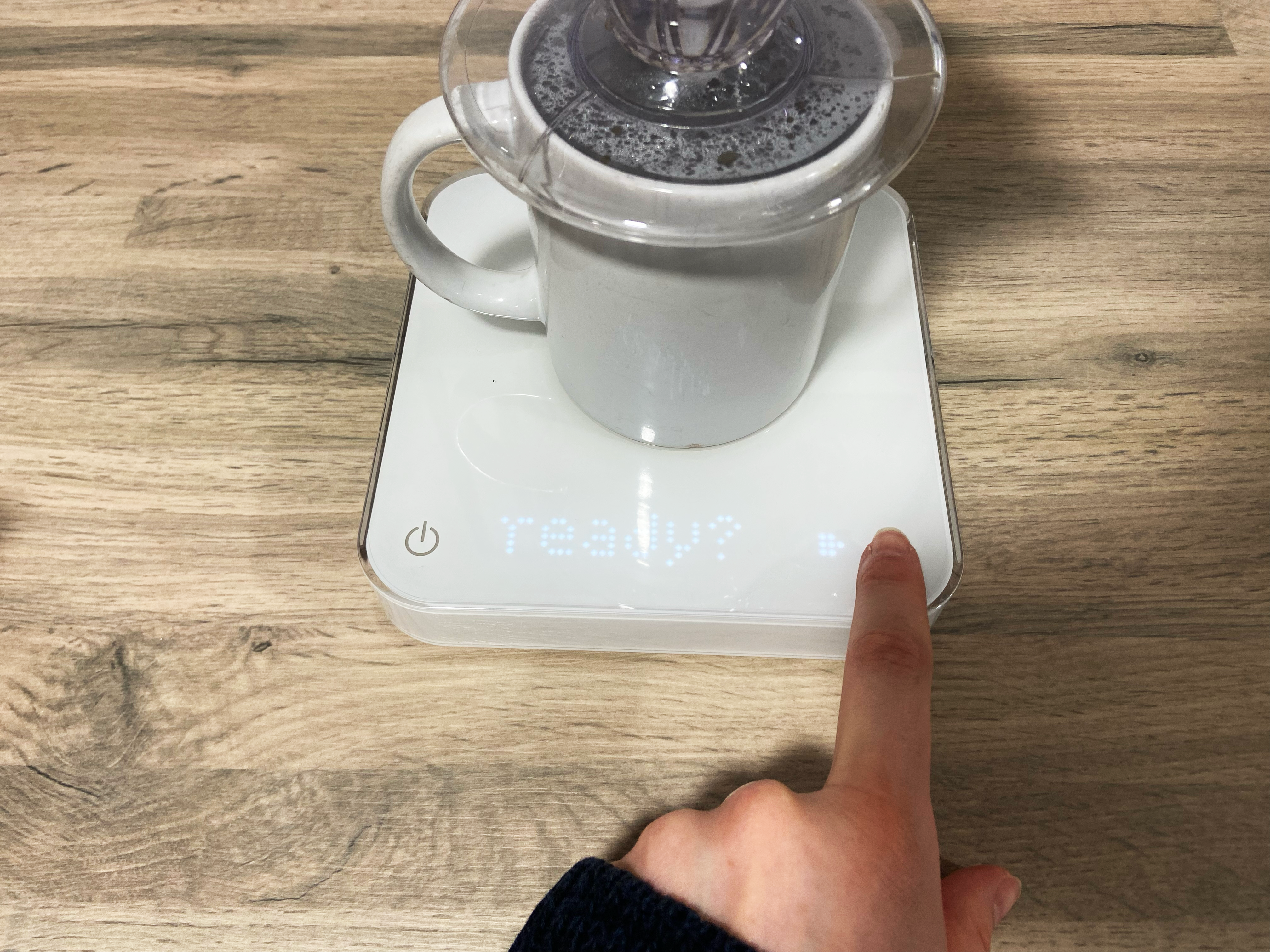 the user pressing tare button on the acaia pearl s coffee scale with a v60 mug on top