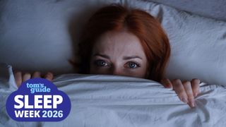 A woman lying on her back in bed, awake at night with the cover pulled up over her chin.