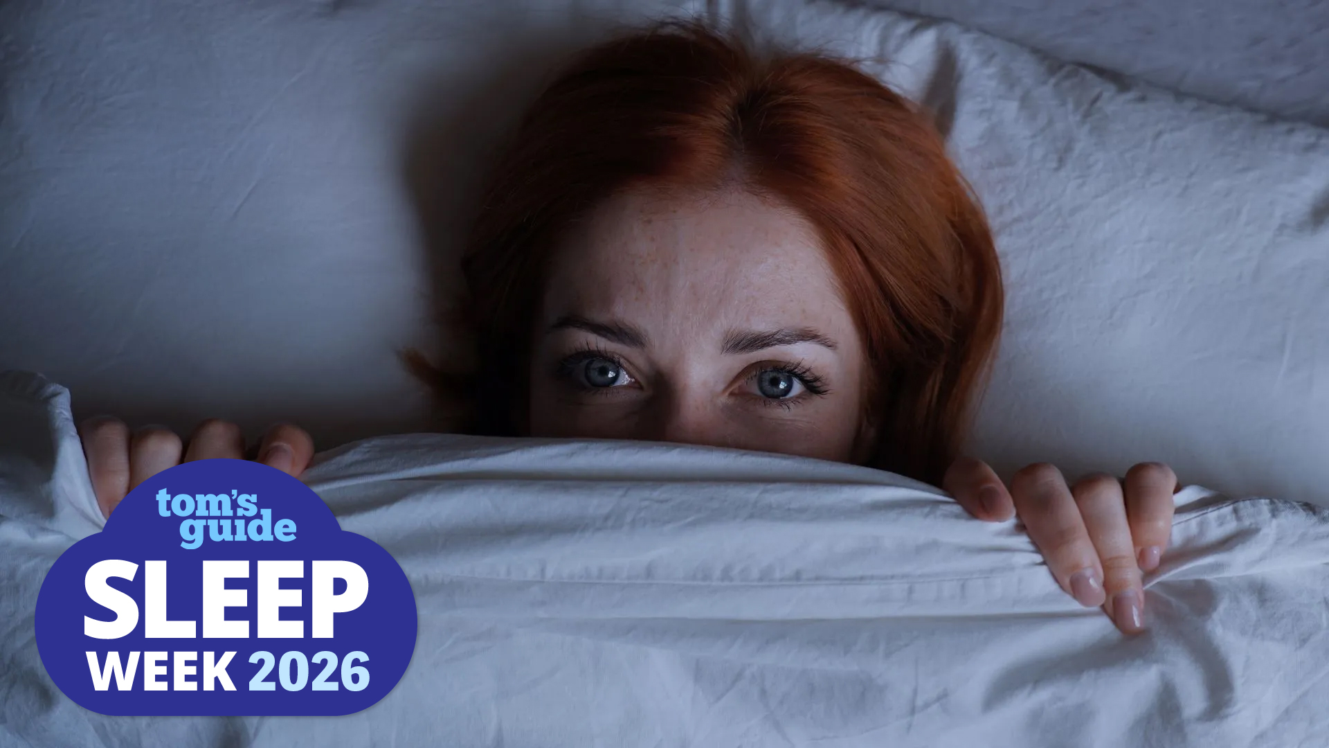 A woman lying on her back in bed, awake at night with the cover pulled up over her chin.