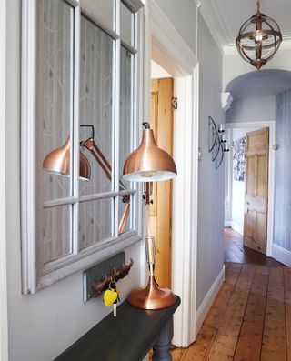 A grey hallway with a window pane mirror and bronze lamp