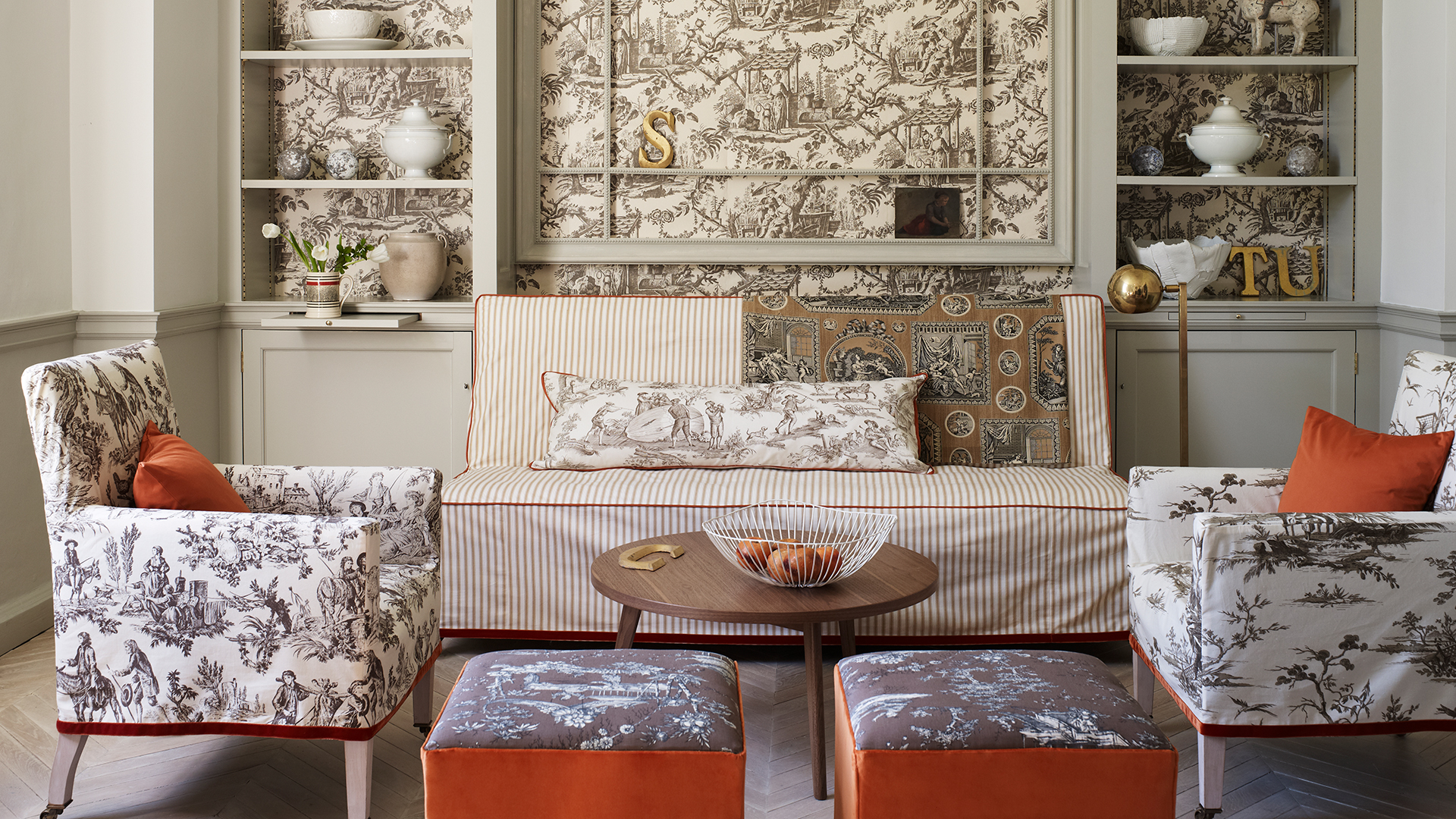 Neutral living room with orange fabrics and toile patterned wallpaper
