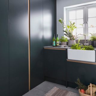 utility room colour ideas, dark blue utility room with sleek modern doors and cabinetry, Belfast sink, plants, rug, grey tiled floor