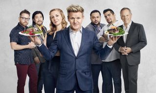 gordon ramsey in a blue suit holding plates of food surrounded by different chefs from Master chef