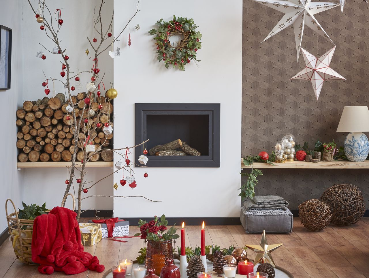 A living room decorated for Christmas with a decorated twig tree, a stack of firewood, and hanging paper star shades