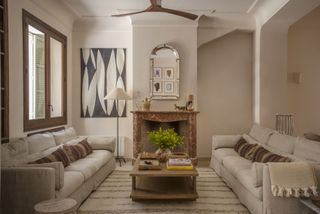 A symmetrical living room with two sofas each other, a marble fireplace, and a floor lamp in the corner