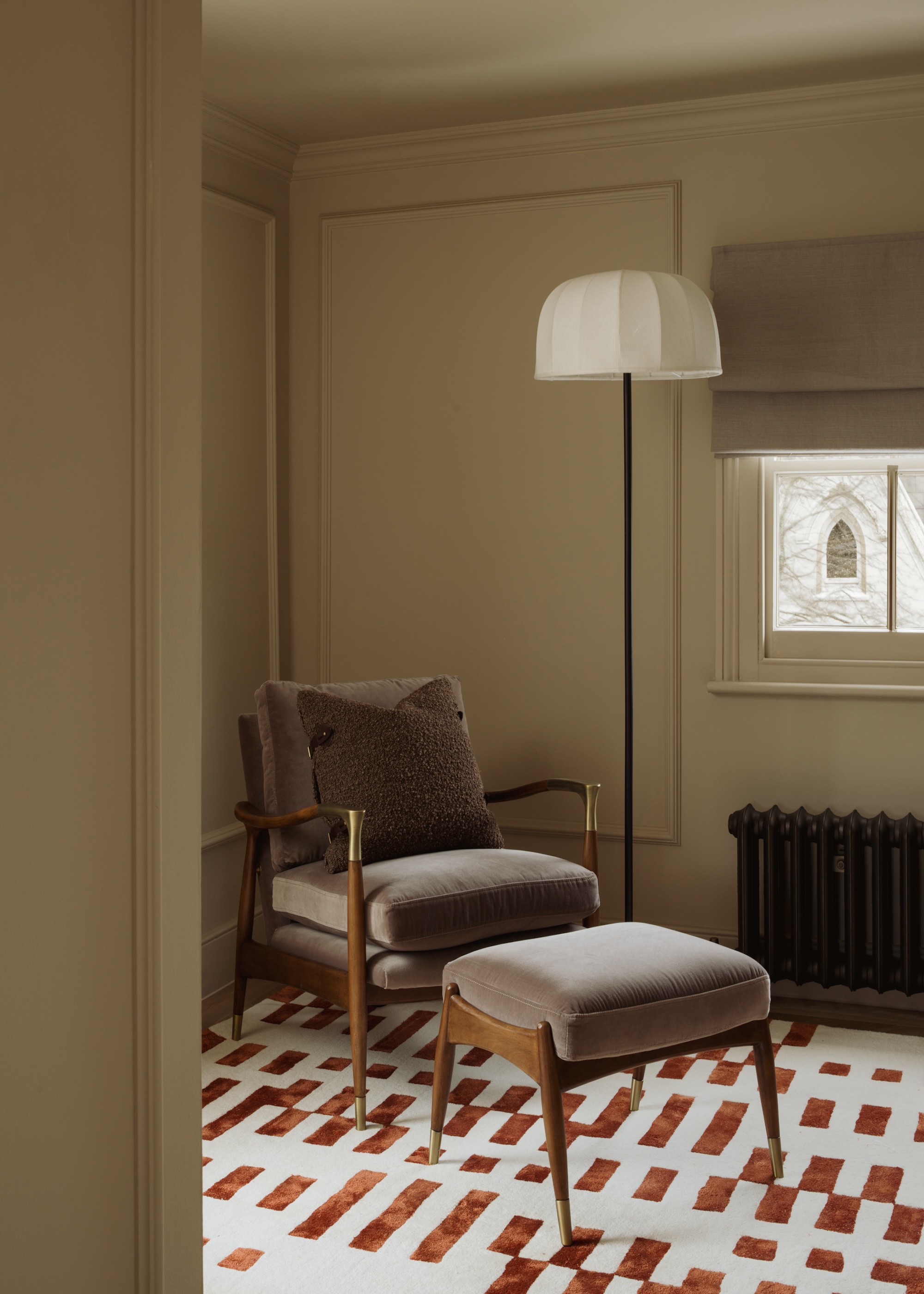 A cosy reading nook with a classic retro style armchair and matching footstool with a neutral floor lamp