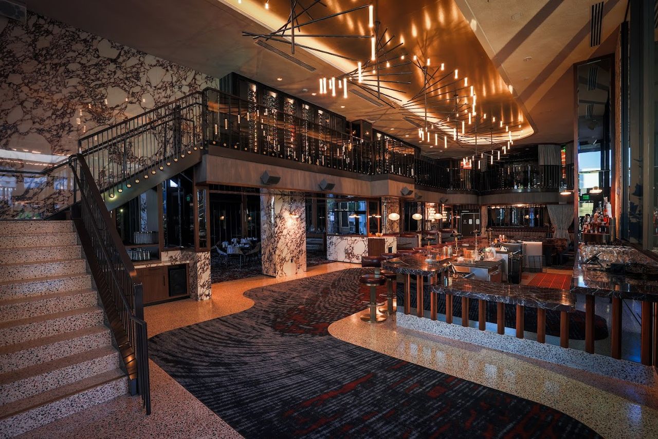 A 1970s-inspired indoor dining room features choreographic lighting, terrazzo surfaces, rugs, and leather and marble accents for a glamorous result.