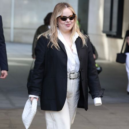 Nicola Coughlan walks down the street wearing white jeans with silver platform heels, a white shirt and a black blazer.