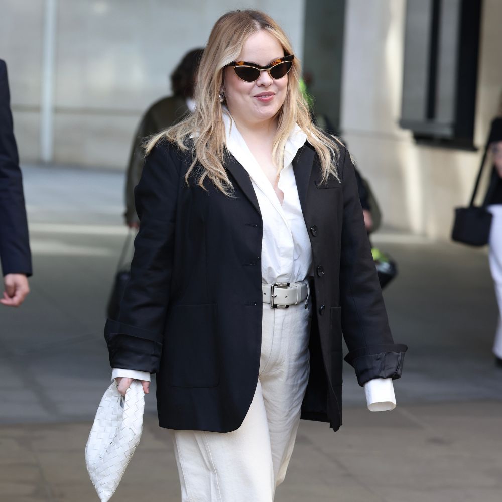 Nicola Coughlan walks down the street wearing white jeans with silver platform heels, a white shirt and a black blazer.