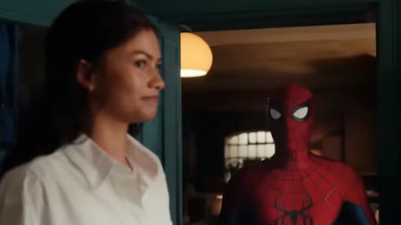 Zandaya in the foreground with a sly smile with Spider-Man (Tom Holland) in a doorway behind her. 