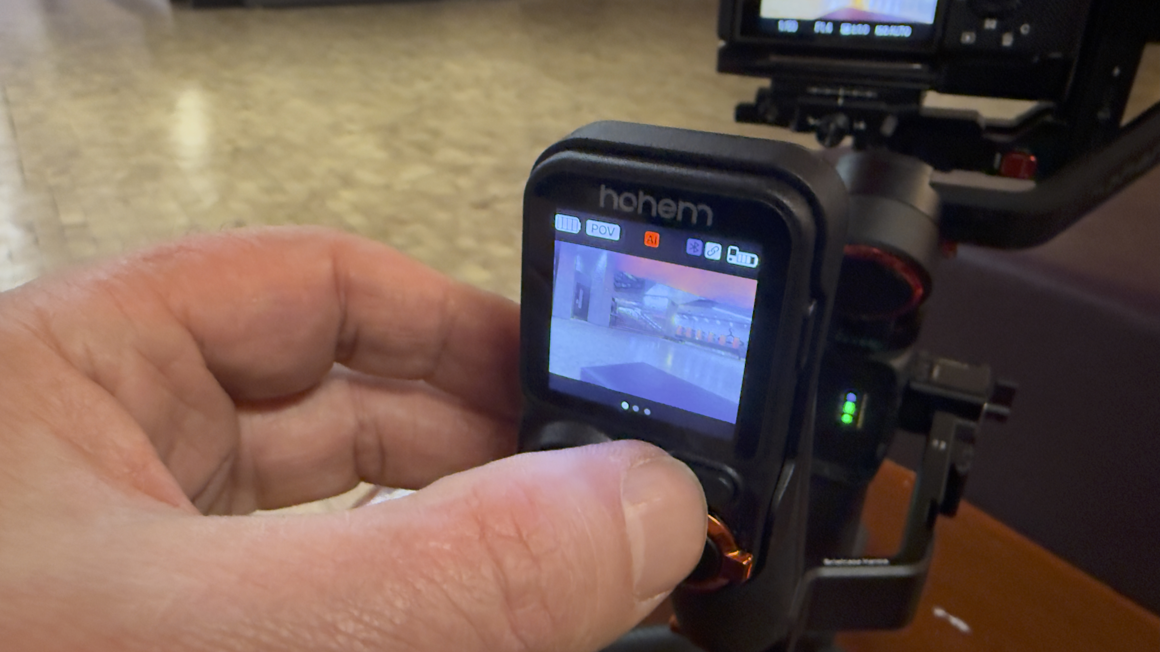 Close-up of the Hohem MT3 remote controller screen showing gimbal modes and camera preview while a hand adjusts the control dial.