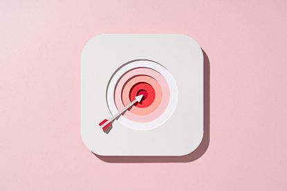 Multi-layered paper craft arrow in shades of white and pink with a bullseye target on red