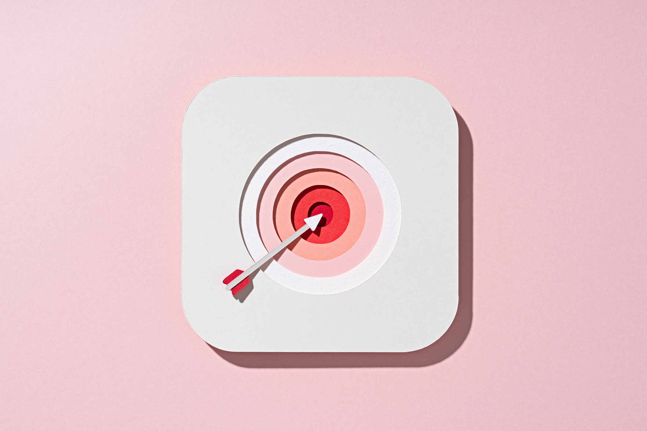 Multi-layered paper craft arrow in shades of white and pink with a bullseye target on red