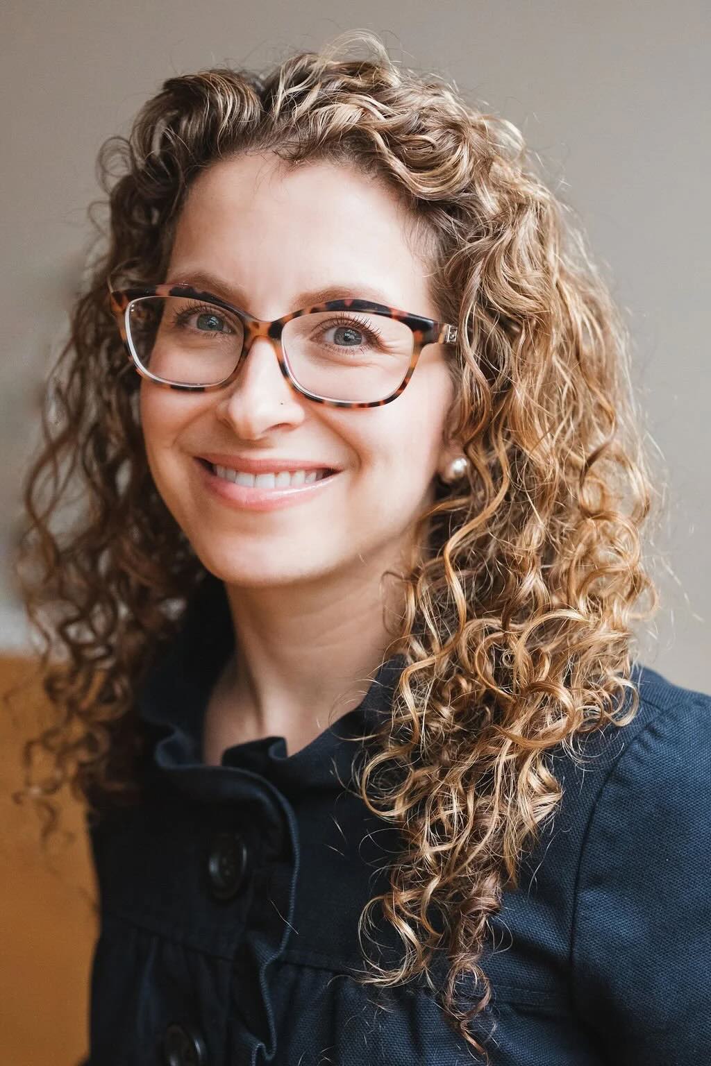 A woman with curly blonde hair, glasses, and a blue blouse smiles for the camera.