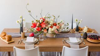 A dining table with a table runner, flowers, and food