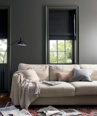 A living room painted in a dark gray color with a beige linen sofa