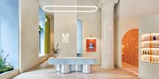An inventively designed, transitional wellness clinic boasts glazed pillars with ornate friezes, plaster walls in matte beige, a central, chrome and marble reception counter, arched walls, and lime green and orange accents.