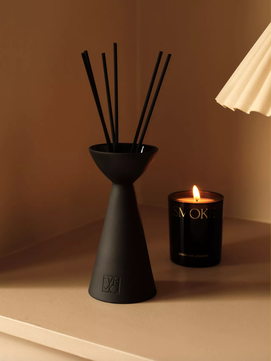 A diffuser by a candle and a white lamp shade
