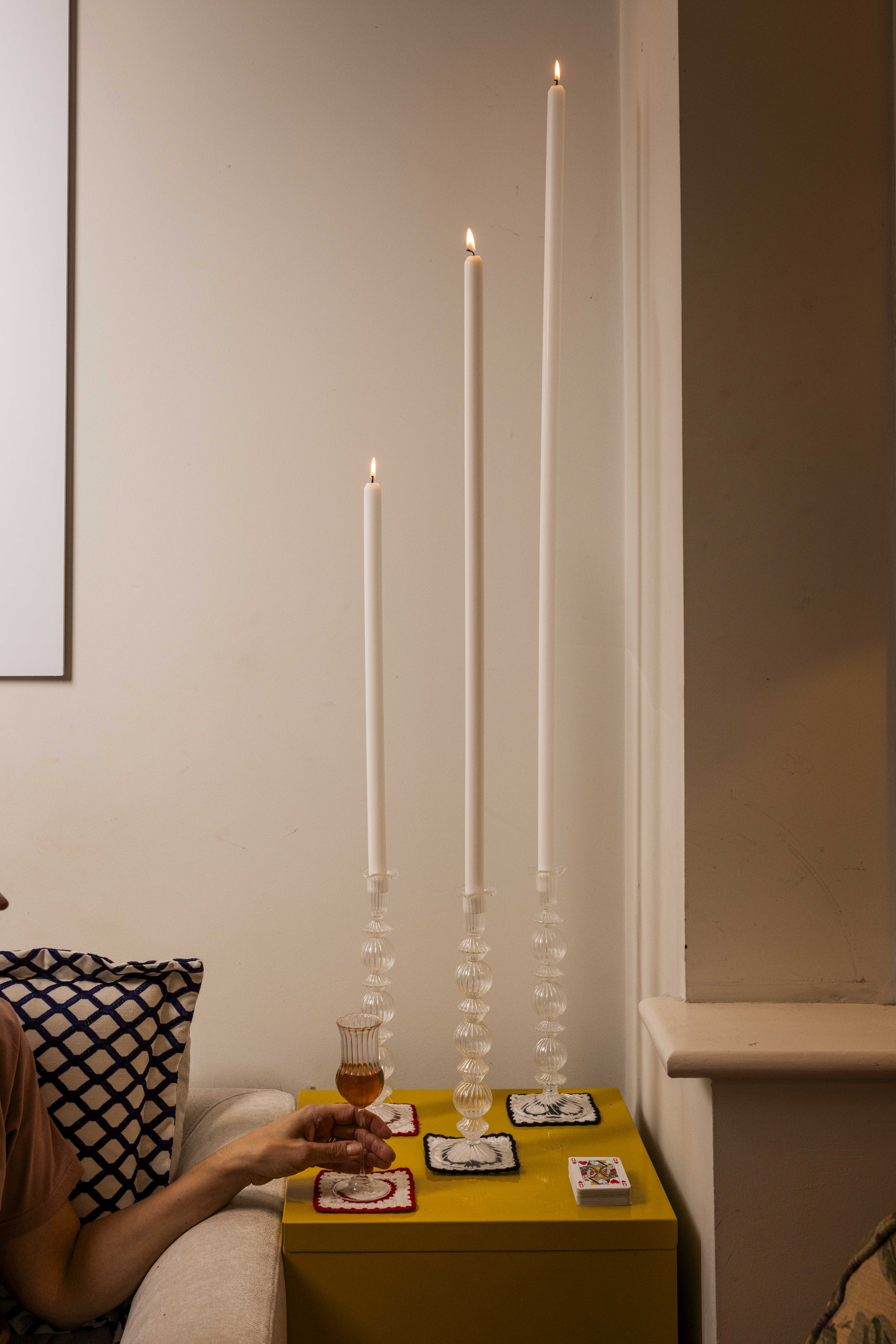 candle holders on a side table with huge candles inside, a woman's hand is seen holding an aperitif glass