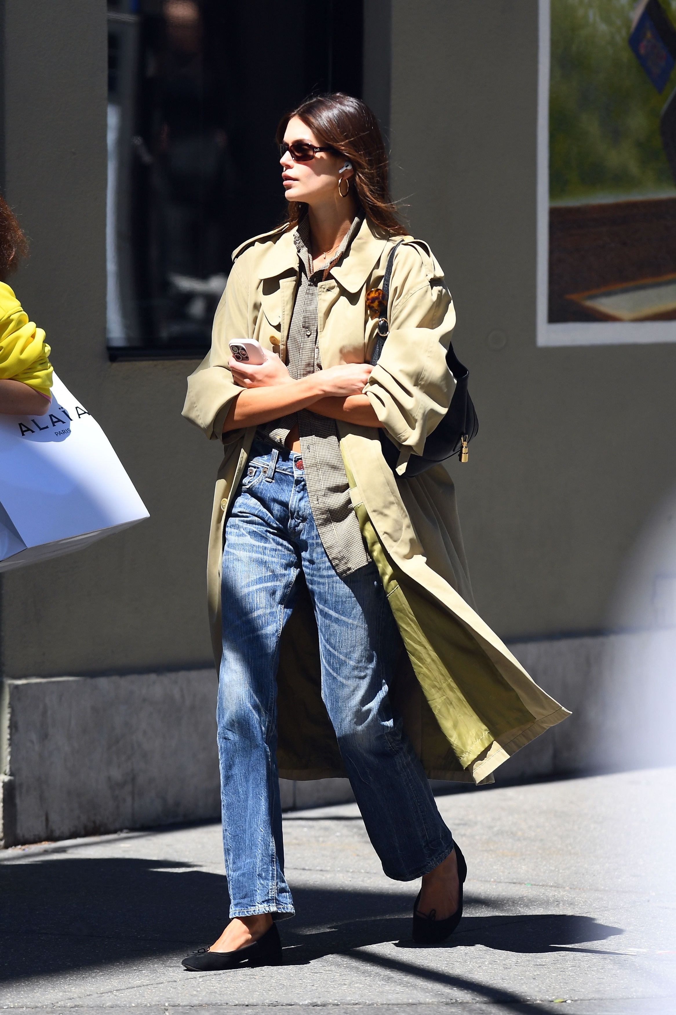 Kaia Gerber wearing a trench coat, a button-down, jeans, and ballet flats