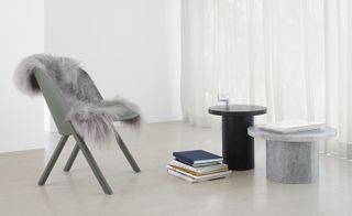 A gray chair with sheepskin on it sits next to two side tables in black and gray marble.