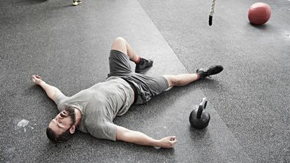 A man lying on the gym floor after a workout looking exhausted