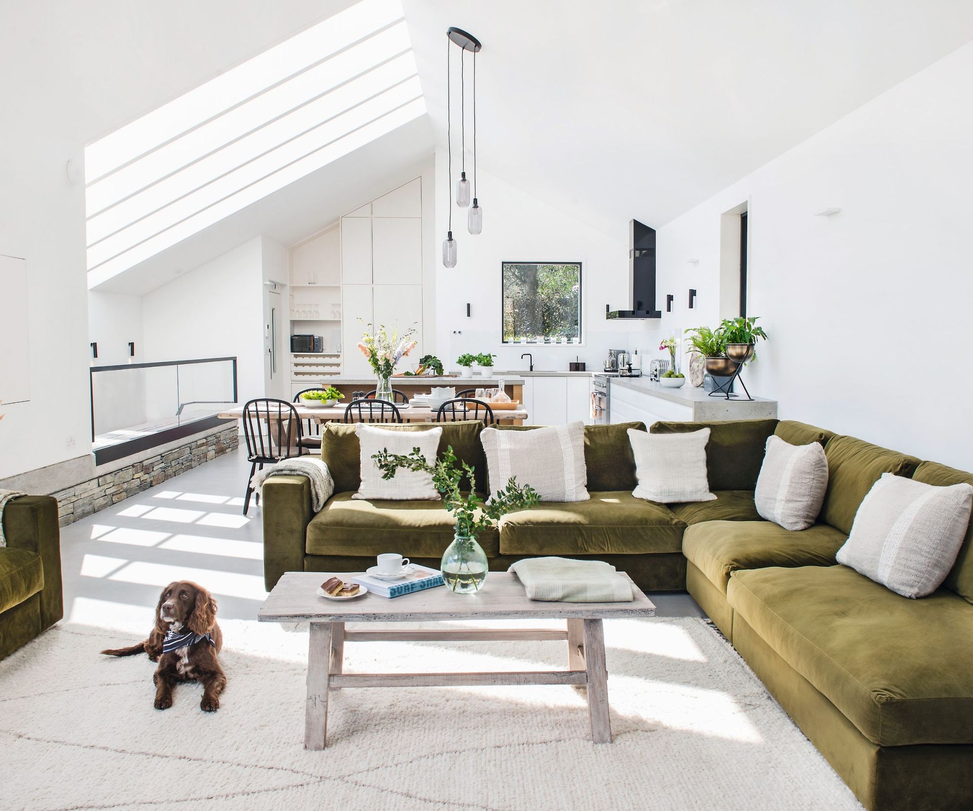 Green velvet sofa, white and grey cushions, wooden table, white rug