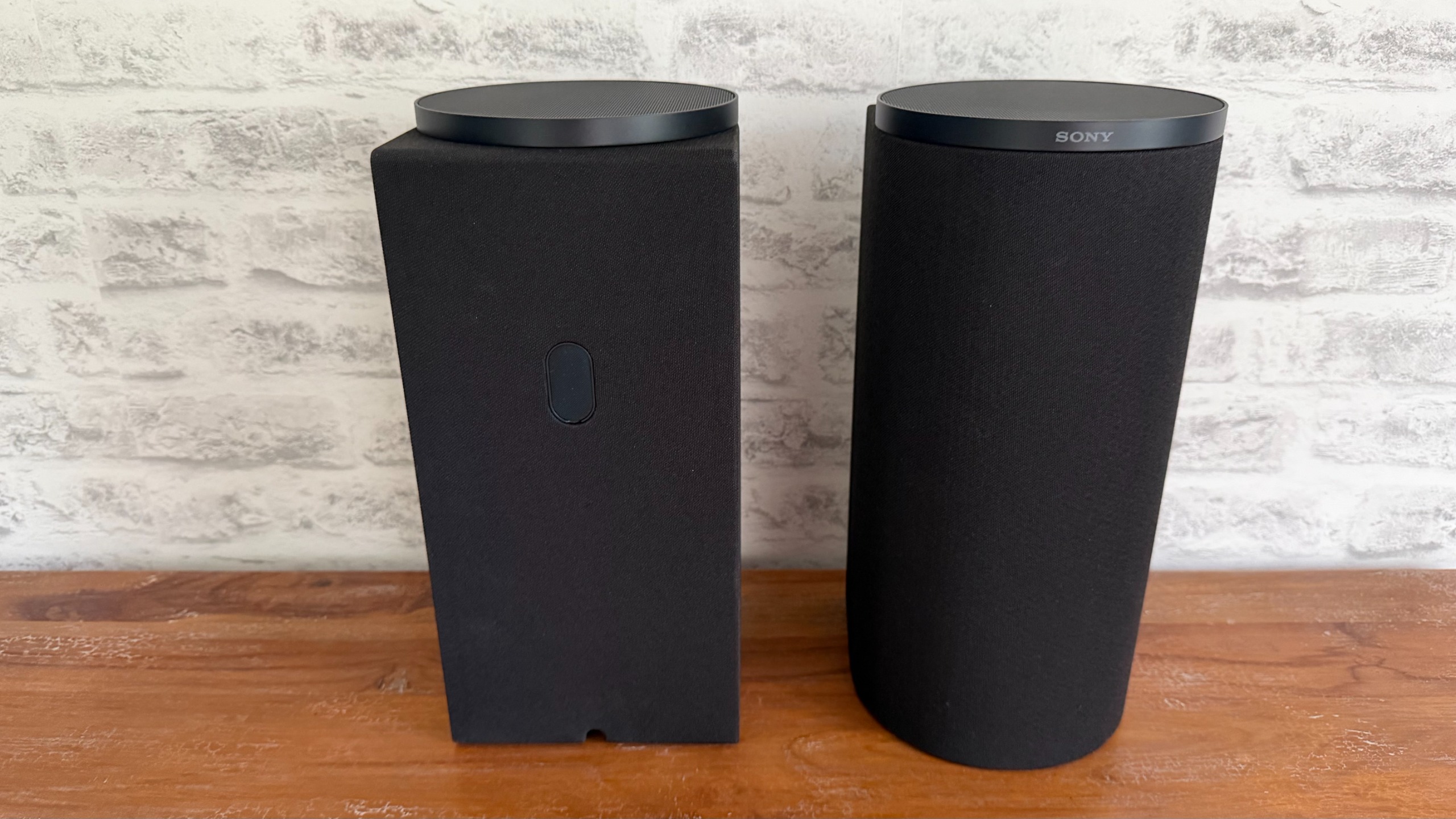 A front and back speaker of the Sony Bravia Theater Trio sit on a wooden sideboard.