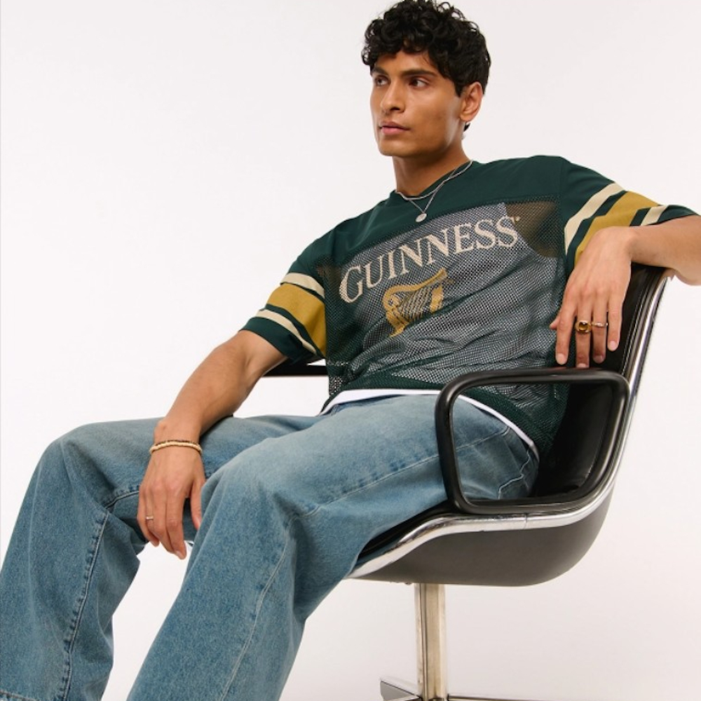 A male model posing on a black desk chair wearing a Guinness top and denim jeans from Abercrombie & Fitch